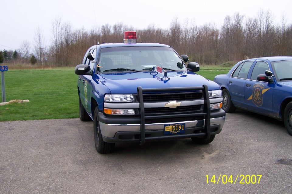 Blue Chevrolet Tahoe police SUV with a push bar and light bar, parked next to a blue Ford Crown Victoria