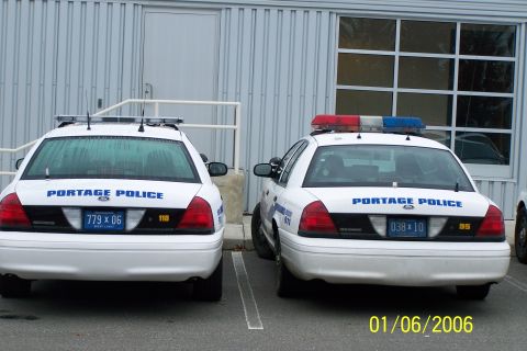 2003 Ford Crown Victoria - Two police vehicles from Portage are parked in front of a building. The vehicle on the right has a light bar with red and blue lights.