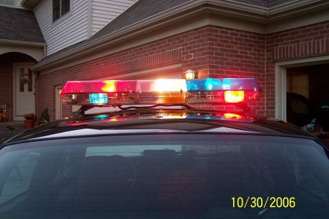 2003 Ford Crown Victoria - A police light bar with red and blue lights is mounted on the roof of a dark-colored vehicle.