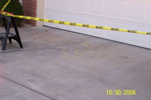 2003 Ford Crown Victoria - Caution tape and a chalk outline are visible on the concrete in front of a garage door.