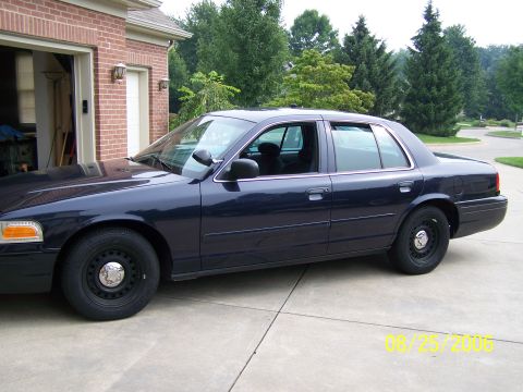 2003 Ford Crown Victoria - A dark blue 2003 Ford Crown Victoria sedan is parked in front of a brick garage.