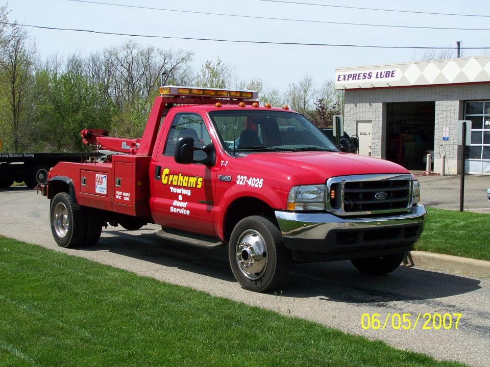 Red tow truck with 'Graham's Towing' logo, parked on a paved surface next to a grassy area