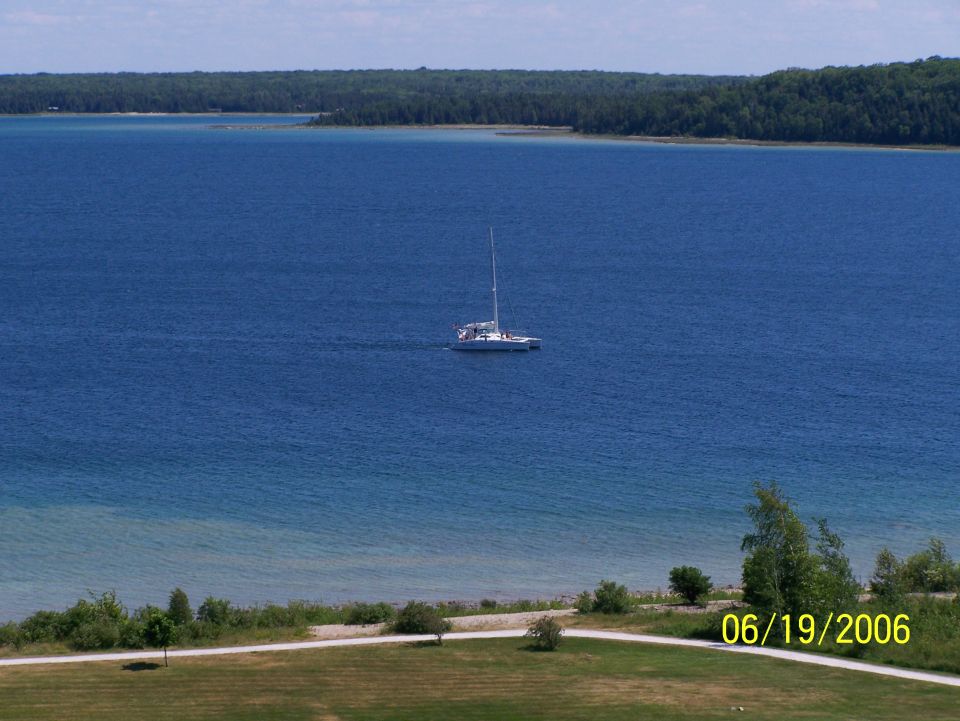 Sailboat on blue water with green shoreline and trees under a blue sky