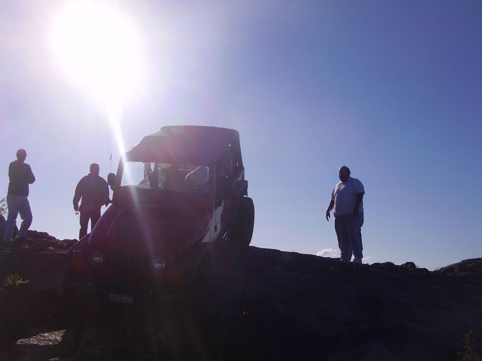 Red off-road vehicle on a rocky incline with people around
