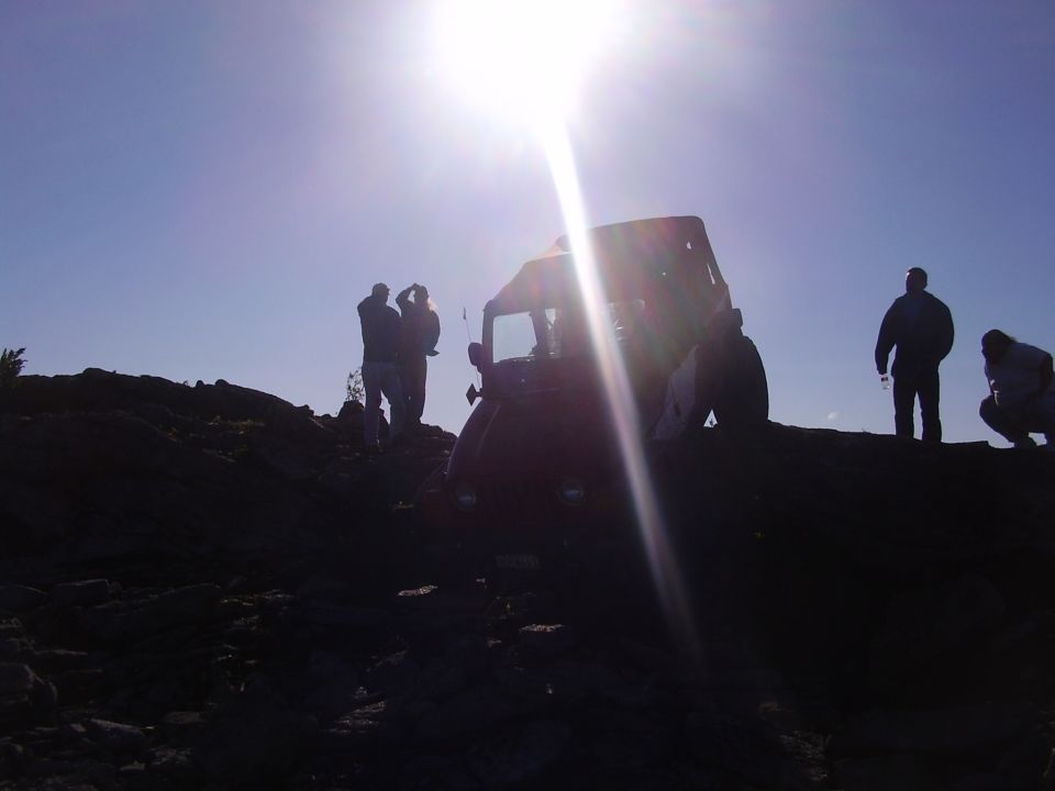 Red Jeep Wrangler on rocky terrain under bright sun