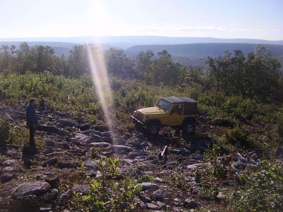 Yellow 2003 Jeep Wrangler on a rocky trail with a person standing nearby