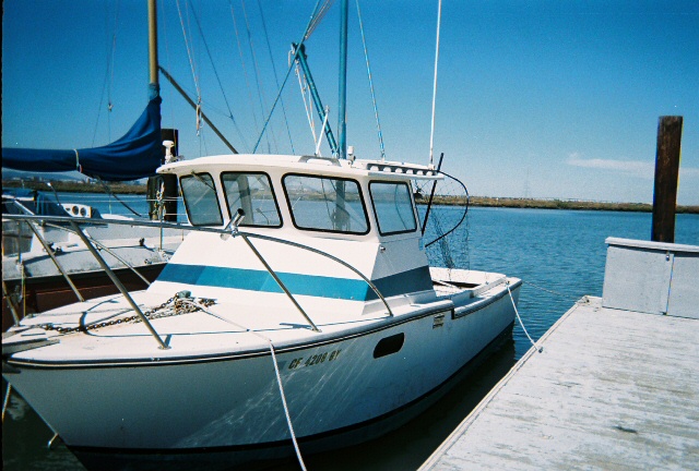 White cabin cruiser boat with blue stripes docked next to a wooden pier