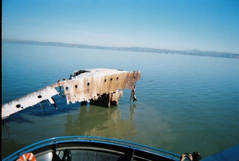 1991 Ford Bronco - A partially submerged ship wreck lies in calm blue water under a clear sky, with a boat visible in the foreground.