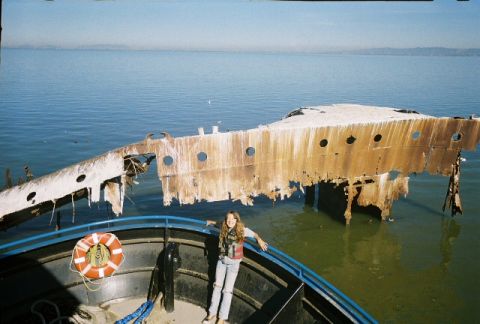1991 Ford Bronco - A girl stands on a boat near a large, decaying shipwreck in the water.