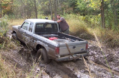 1978 Ford Bronco - A man watches as a silver Ford pickup truck gets stuck in the mud on an off-road trail.