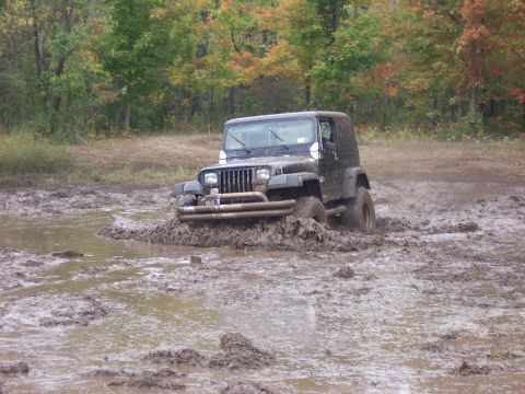 1978 Ford Bronco - A black Jeep Wrangler is stuck in a muddy off-road area with trees in the background.