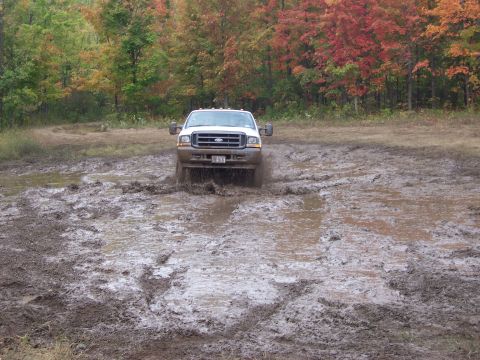 1978 Ford Bronco - A white Ford F-250 Super Duty navigates a muddy obstacle course during autumn.
