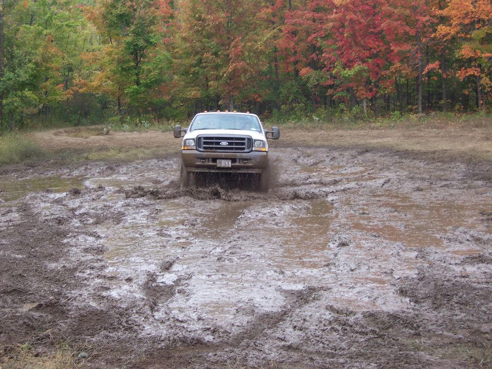 White Ford F-250 Super Duty driving through mud puddle, front view. Year 2004