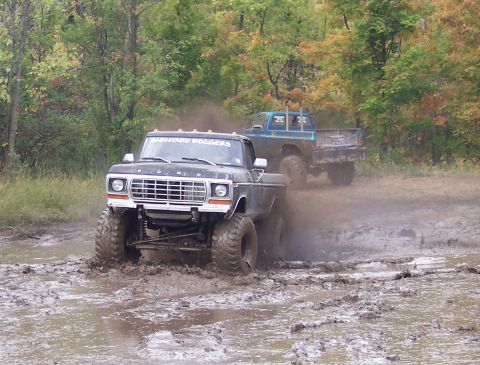 1978 Ford Bronco - Two lifted trucks navigate a muddy off-road course during the fall.