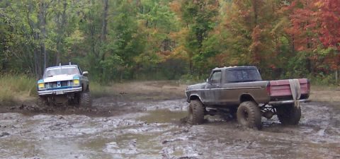 1978 Ford Bronco - Two modified trucks navigate a muddy off-road course during autumn.