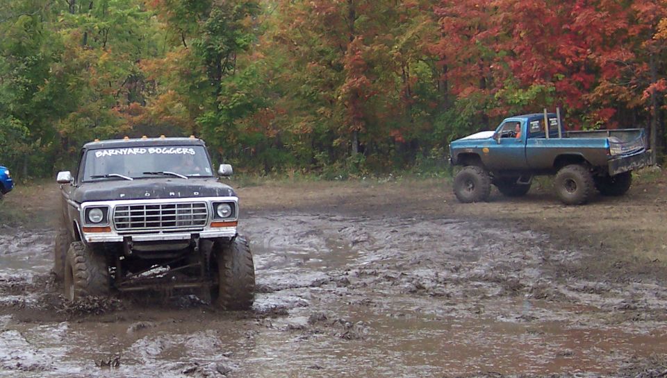 Front view of a dark SUV driving through mud with another vehicle behind