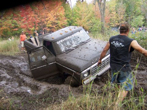 1978 Ford Bronco - An SUV is stuck in the mud with a person attempting to push it free.