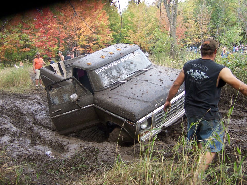 SUV stuck in mud, person trying to push it out
