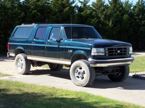 1995 Ford C-150 (Centurion Conversions) - A dark green Ford Bronco SUV is shown from a three-quarter front angle, parked outdoors on a sunny day.