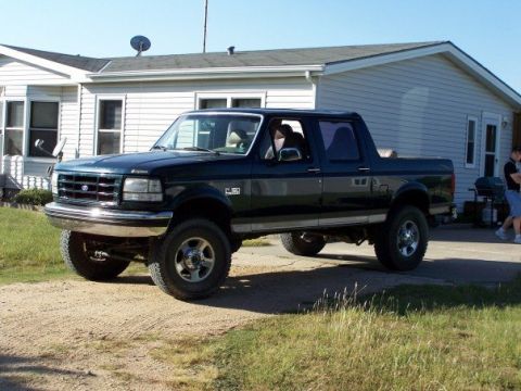 1995 Ford C-150 (Centurion Conversions) - A dark-colored pickup truck is parked outside a building on a sunny day.
