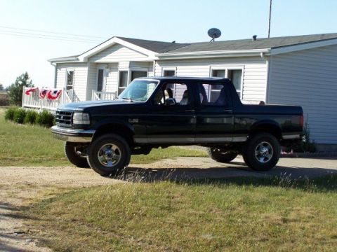 1995 Ford C-150 (Centurion Conversions) - Side view of a black pickup truck parked outdoors near a building.