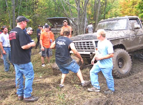 1978 Ford Bronco - Several people gather around a mud-covered 1978 Ford Bronco that appears to be stuck off-road.