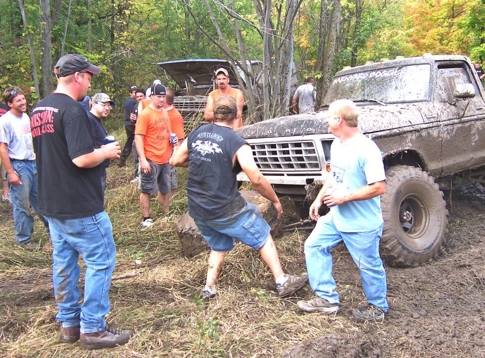 Muddy 1978 Ford Bronco stuck in off-road terrain with people attempting to free it