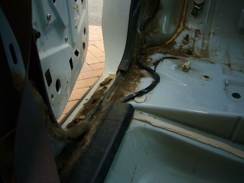 2001 Ford Crown Victoria - The interior of a car shows dirt and exposed wiring near the door sill and floor.