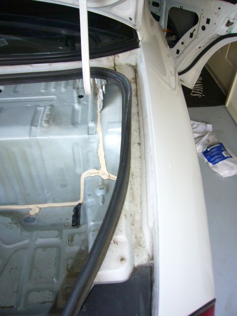 2001 Ford Crown Victoria - The interior of a white car's trunk shows exposed metal and sealant, suggesting it is undergoing some form of maintenance or repair.