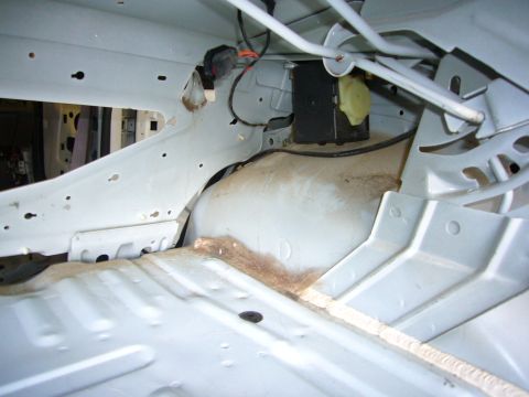2001 Ford Crown Victoria - The bare metal interior of a vehicle shows structural components and wiring, with some dust and debris.