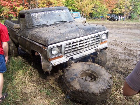 1978 Ford Bronco - A heavily mud-caked pickup truck is stuck in a muddy field, with one tire off the ground.