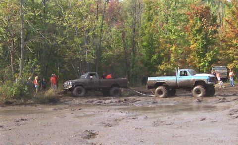 1978 Ford Bronco - Two pickup trucks are stuck in the mud, with one attempting to tow the other out.