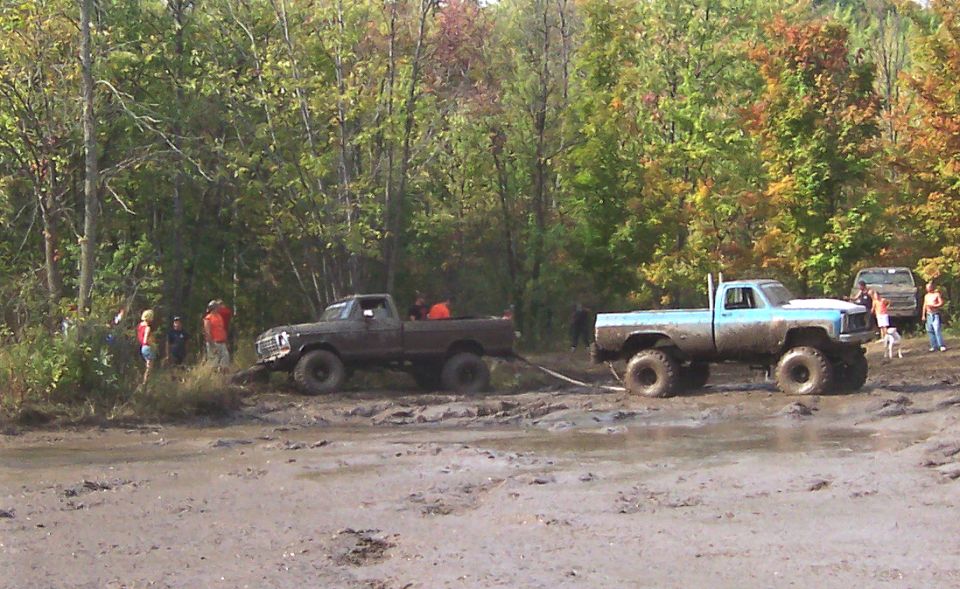 Light blue pickup truck being pulled by a dark pickup truck in mud