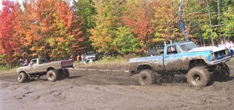 1978 Ford Bronco - Two heavily modified pickup trucks navigate a muddy terrain during an off-road event.
