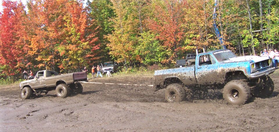 Muddy blue pickup truck towing a brown pickup truck, with fall foliage