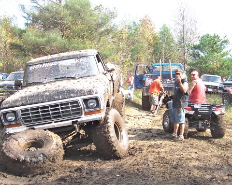 1978 Ford Bronco - A group of people and several off-road vehicles are gathered in a muddy area with trees in the background.