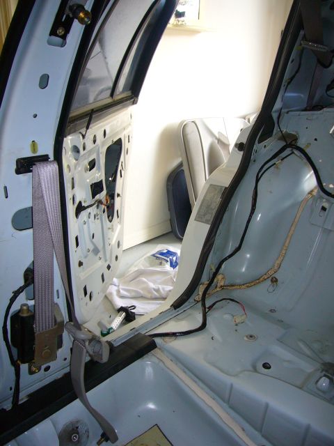 2001 Ford Crown Victoria - The interior of a 2001 Ford Crown Victoria is shown with the door panel removed, revealing the seatbelt mechanism and internal wiring.