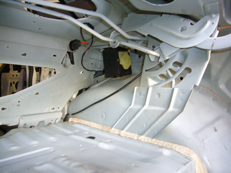 Car interior structure with exposed metal panels, wiring, and a black box. The floor is visible