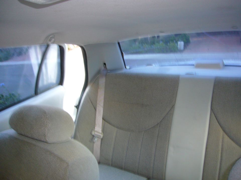 Back seat interior of a car with beige fabric seats and a white seatbelt