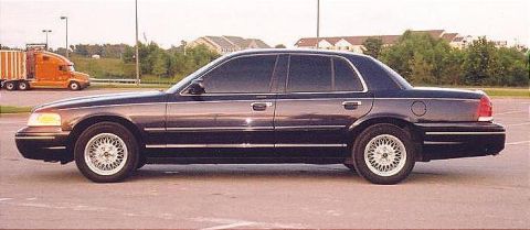 1999 Ford Crown Victoria - Dark blue Ford Crown Victoria sedan parked on asphalt with a semi-truck in the background.