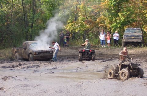 1978 Ford Bronco - A truck appears to be stuck and smoking in a muddy off-road area, with ATVs and spectators present.