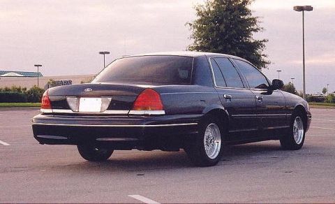 1999 Ford Crown Victoria - The rear of a dark blue sedan is shown in a parking lot with a tree and streetlights in the background.