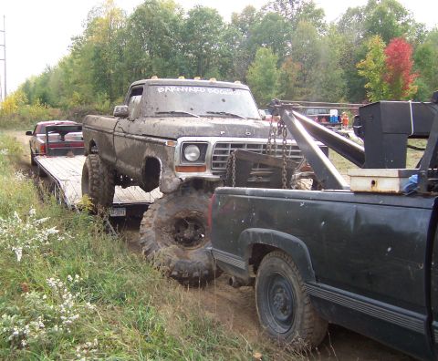 1978 Ford Bronco - A heavily mud-covered 1978 Ford F-Series pickup truck is being loaded onto a tow truck, with another vehicle and trailer visible in the bac…