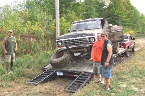 1978 Ford Bronco - Muddy 1978 Ford Bronco loaded onto a trailer, with two men watching. Another truck is visible on the trailer.