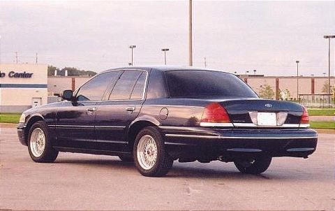 1999 Ford Crown Victoria - A dark sedan is parked in front of a building, viewed from the rear three-quarter angle.