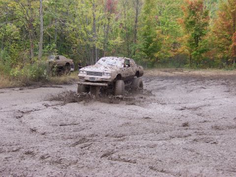 1978 Ford Bronco - Two heavily modified trucks power through a muddy off-road course during a fall day.