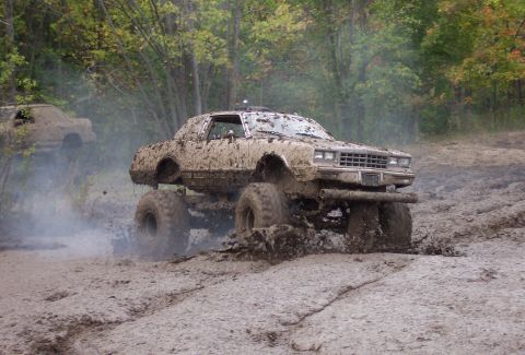 1978 Ford Bronco - A heavily modified car, covered in mud, navigates a challenging off-road course with another vehicle visible in the distance.