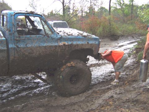 1978 Ford Bronco - A blue pickup truck is stuck in the mud with a person inspecting its front end.