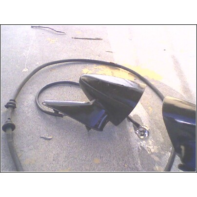 1973 Ford Ranchero - A black side mirror assembly with a cable is shown on a concrete surface, likely a part from a vehicle.