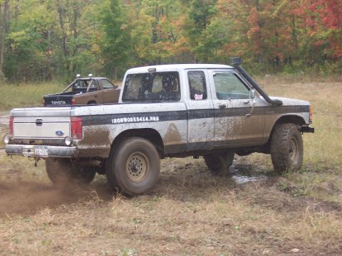 1978 Ford Bronco - Off-road pickup truck covered in mud, with a snorkel installed for water crossings. Another truck is in the background.